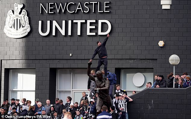 A fan stands on the shoulders of the statue of Alan Shearer and points to the sky in imitation of the Geordie legend's trademark goal celebration