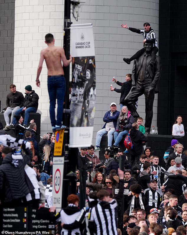 A Newcastle fan sits on the shoulders of the statue of Sir Bobby Robson outside St James' Park