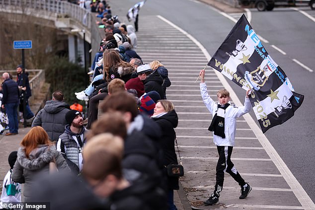 A Newcastle fan waves a flag in the road as fans sit on an overpass to watch the open top bus parade pass