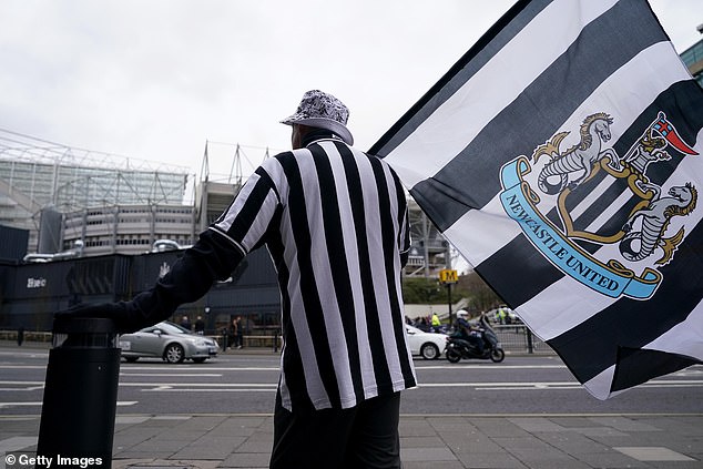 A Newcastle United fan in the club's black and white jersey holds a giant flag bearing the team's crest