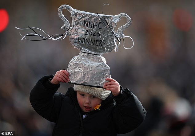 A young Newcastle United fan carries a homemade trophy above his head reading 'NUFC 2025 winners'