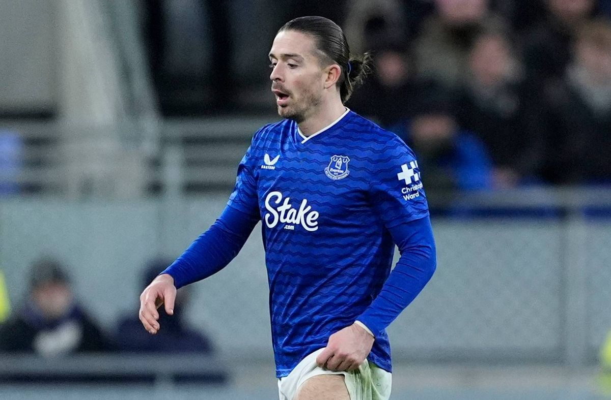An individual dressed in a blue jersey, with the word "Sky" prominently displayed on the front, is actively engaged in a soccer match on a field. The player appears to be in motion, running towards the left side of the image. In the background, spectators can be seen seated on a tiered structure, some of whom are wearing jackets and caps. The setting suggests a well-attended sporting event.