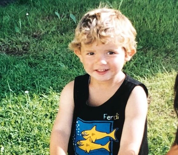 Young Ferdi Kadioglu smiling while wearing a black tank top with two yellow fish and his name on it.