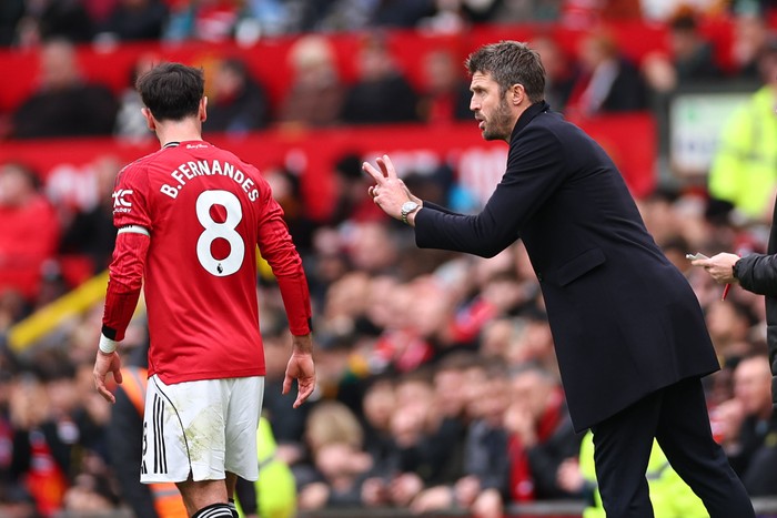 Bruno Fernandes Michael Carrick Michael Carrick, in a black jacket, gestures to Bruno Fernandes, in red and white Man Utd football kit, on the touchline at Old Trafford.