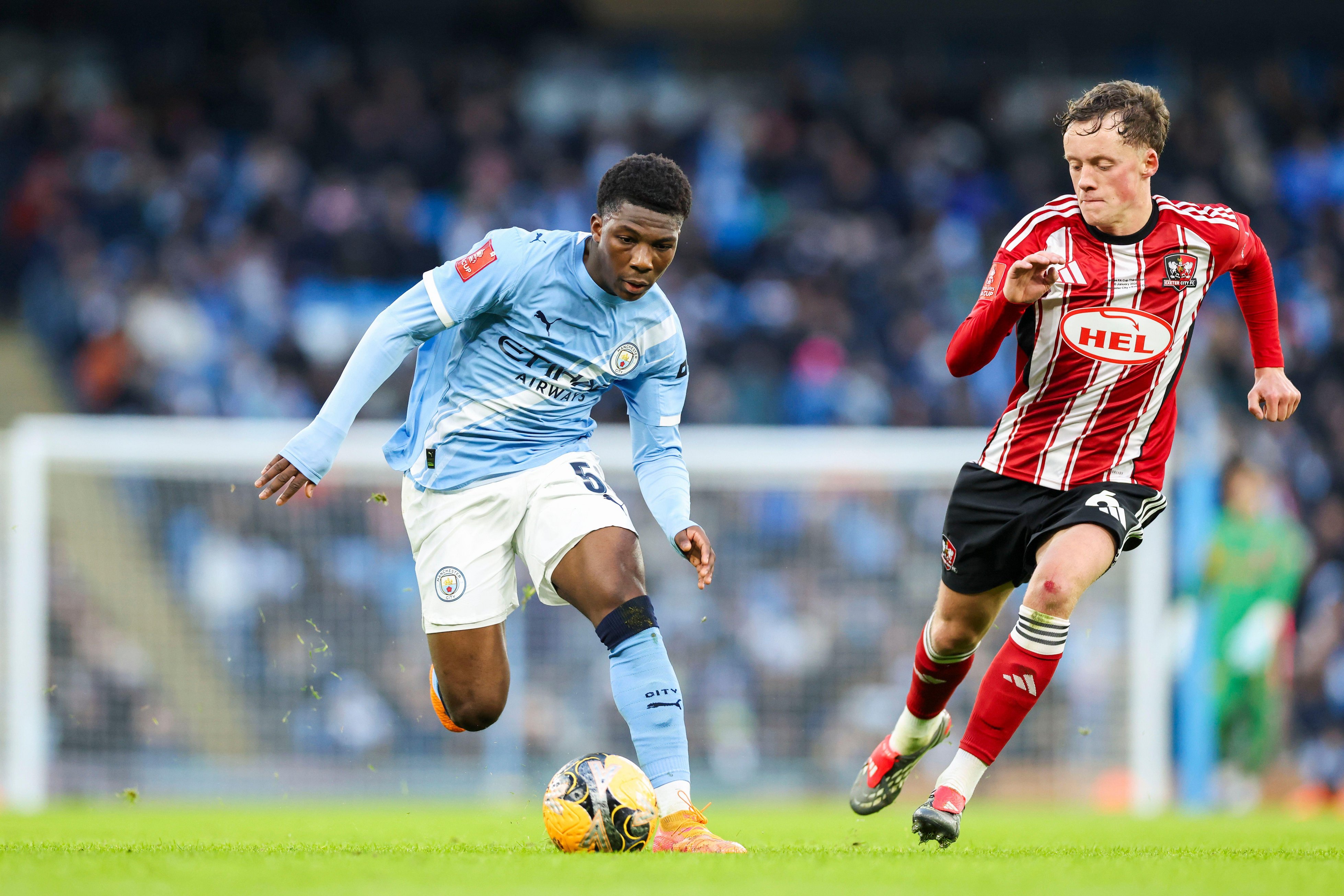 Manchester, UK. 10th Jan, 2026. Manchester City forward Ryan McAidoo (56) battles with Exeter City midfielder Ethan Brierley (6) during the Manchester City v Exeter City Emirates FA Cup Third Round match at the Etihad Stadium, Manchester, England on