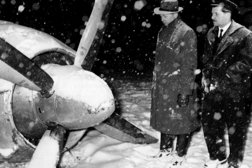 Two men look at an airplane propeller in the snow