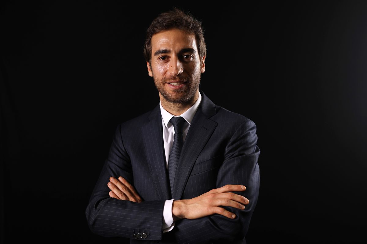 Mathieu Flamini in a suit smiling and posing with his arms crossed