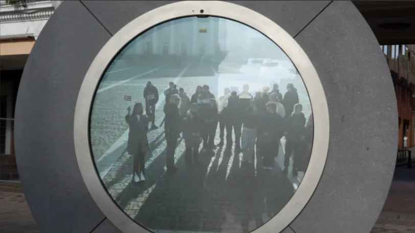 A circle portal stood in the middle of the image. It is made out of silver material and has a screen in the middle showing people standing in it.