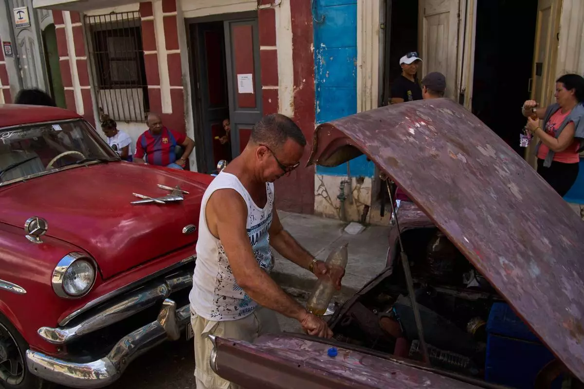 A man finishes putting fuel in his car's tank, located in the back of the car, during a blackout in Havana, Cuba, Monday, March 16, 2026. (AP Photo/Ramon Espinosa)