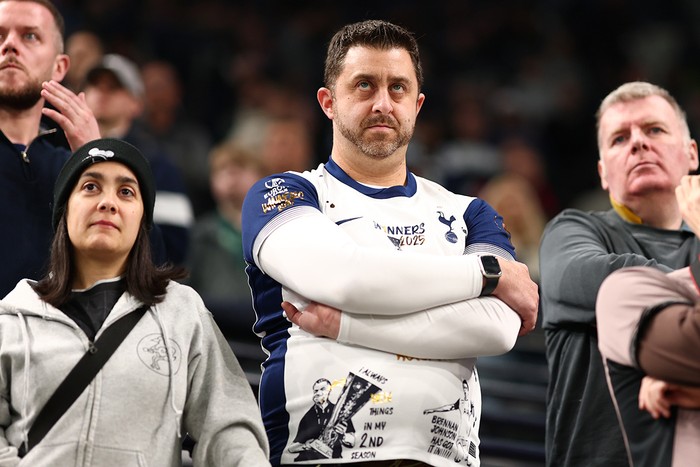A Tottenham fan wearing a customised white home shirt folds his arms and looks unhappy