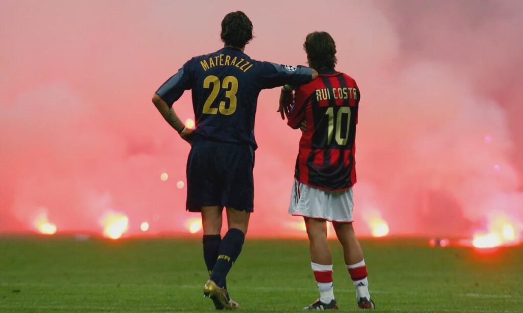 Today is the AC Milan - Inter derby. Let's remember the iconic photo of Marco Materazzi and Rui Costa standing on the pitch while the stands burned during the 2005 Champions League quarterfinal at San Siro.
