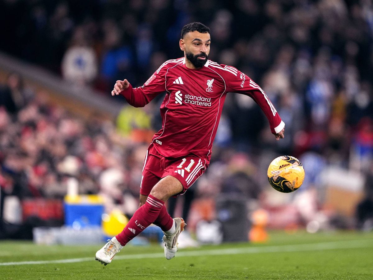 A soccer player in a red uniform is actively engaged in a match, skillfully controlling the ball and running across the field, with a lively crowd in the background.
