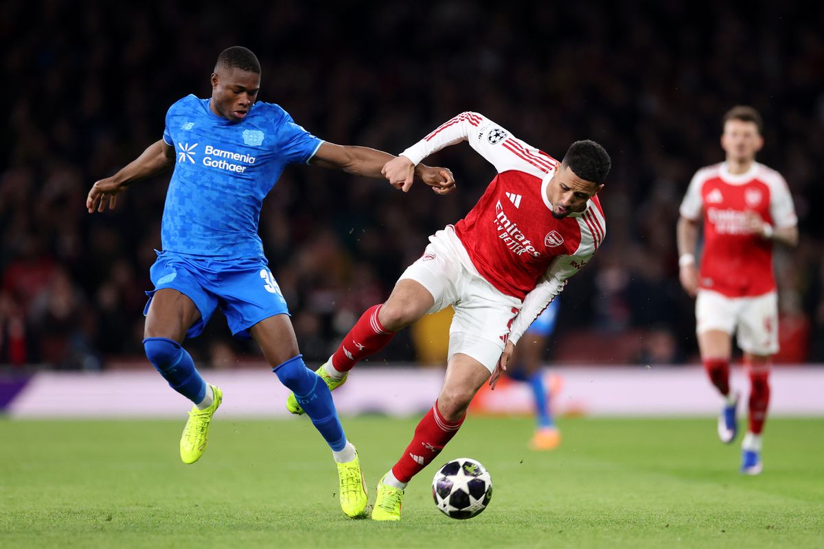 William Saliba of Arsenal is challenged by Christian Kofane of Bayer 04 Leverkusen during the UEFA Champions League 2025/26 Round of 16 Second Leg match between Arsenal FC and Bayer 04 Leverkusen