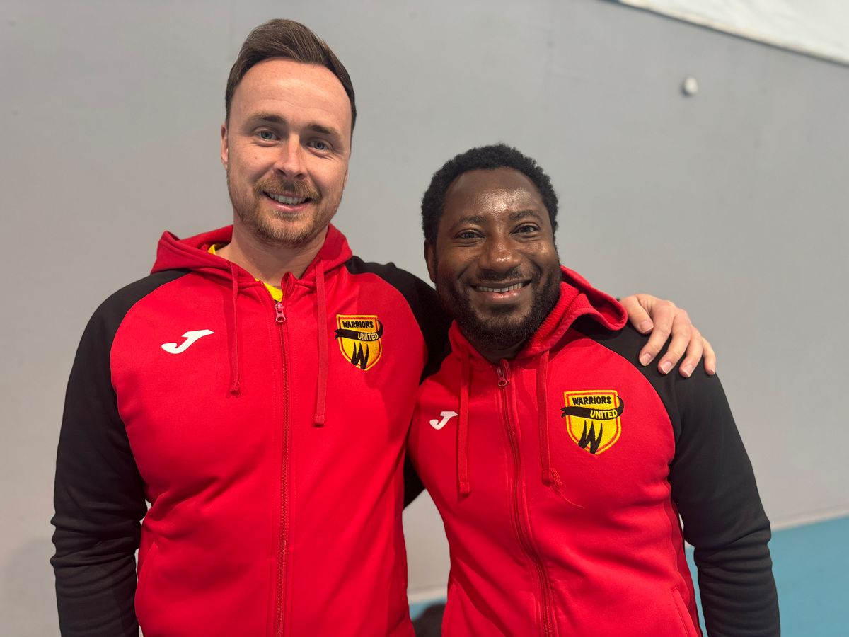 Two men, football coaches, pictured together with Warriors United football kits on