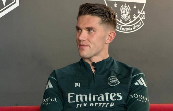 An individual in a green jersey, presumably a sports team's official attire, is seated on a red bench in front of a gray wall ad