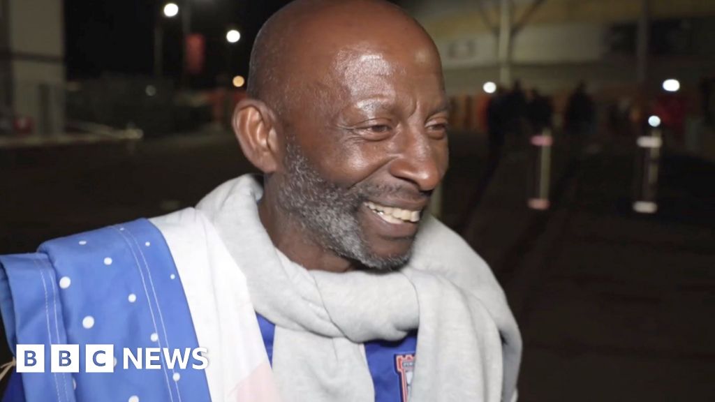 Ipswich Town fan smiles outside the Southampton ground at night. He is wearing a club shirt.