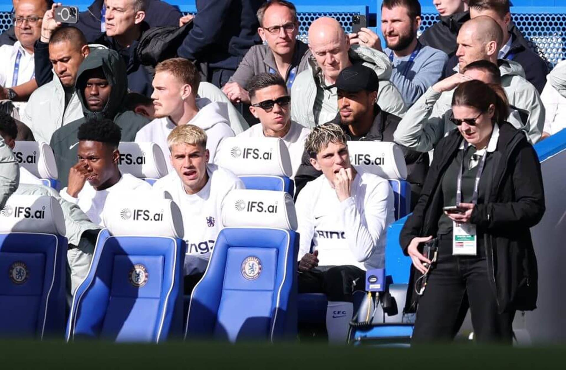 Enzo Fernandez, wearing dark sunglasses, watches Chelsea's defeat to Manchester City from the dugout at Stamford Bridge.