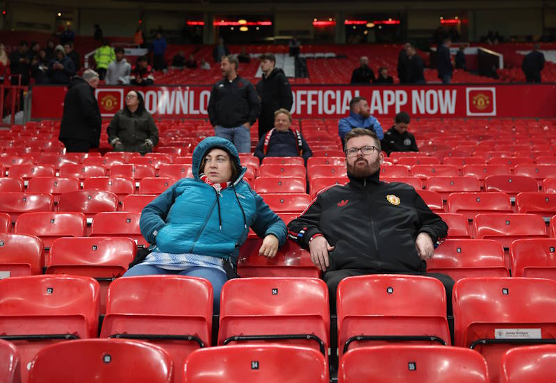 Manchester United fans sit in the stands at Old Trafford with empty seats around them