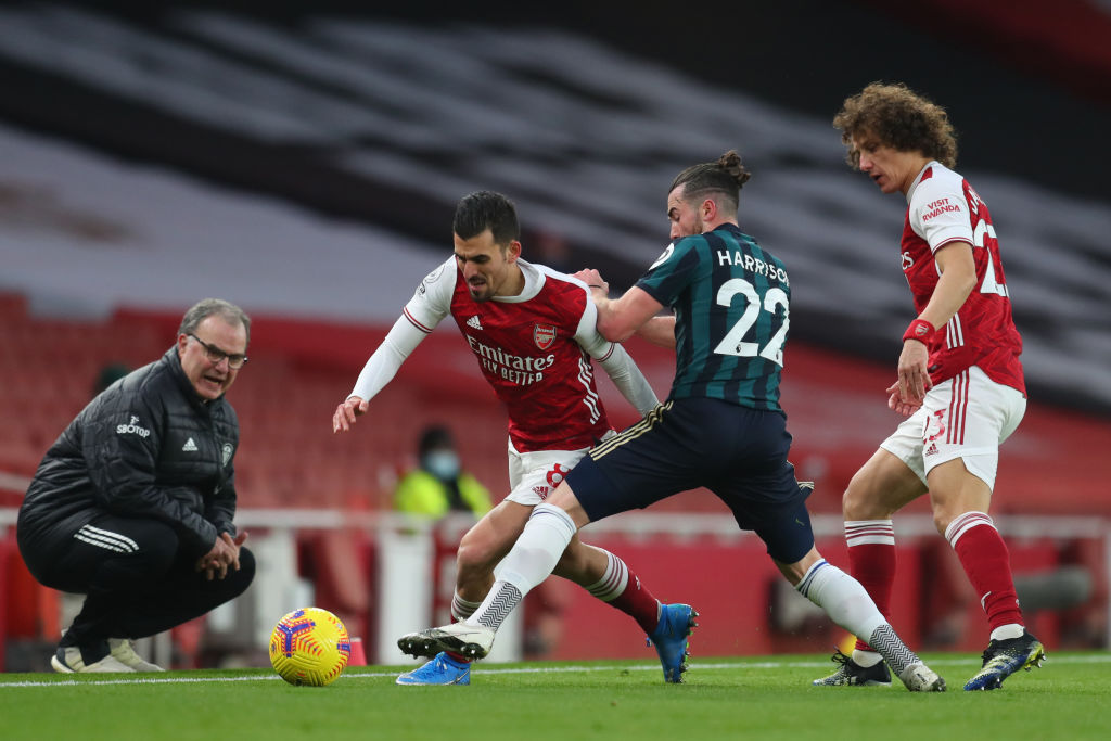 Dani Ceballos of Arsenal is challenged by Jack Harrison of Leeds United as Marcelo Bielsa, Manager of Leeds United looks on during the Premier League match between Arsenal and Leeds United at Emirates Stadium on February 14, 2021 in London, England. Sporting stadiums around the UK remain under strict restrictions due to the Coronavirus Pandemic as Government social distancing laws prohibit fans inside venues resulting in games being played behind closed doors.
