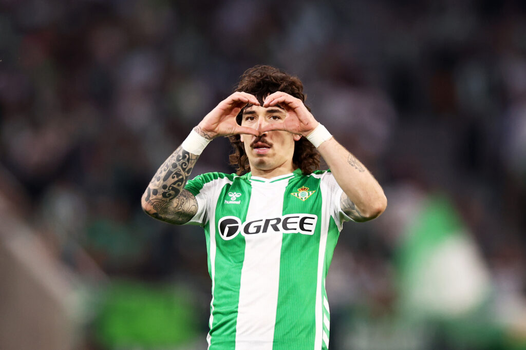 Hector Bellerin, with long curly hair and a big moustache, makes a heart sign with his hands in front of his face after scoring for Real Betis