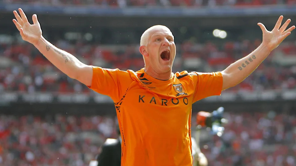 Dean Windass with short, cropped dyed blonde hair celebrates his goal for Hull City against Bristol City with his arms spread wide above his head and wearing an orange Hull City shirt